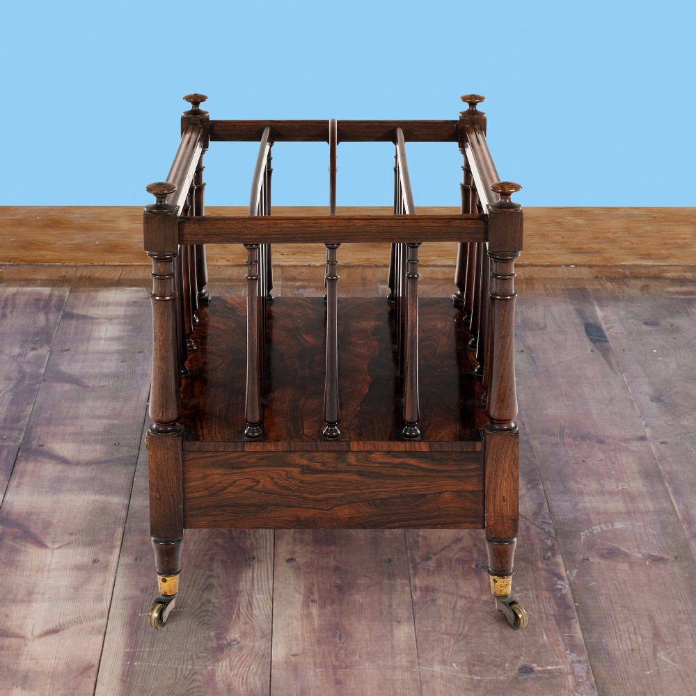 A Victorian rosewood music canterbury featuring turned spindle dividers, a top carrying handle, a lower drawer with two brass knobs, and turned legs with brass castors. View V