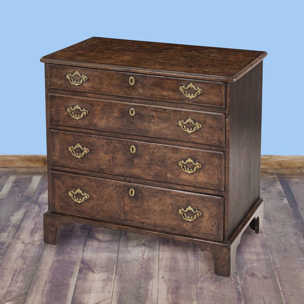 A George II period burr elm chest of drawers featuring four graduated drawers with feather banding, brass handles, and bracket feet. View III
