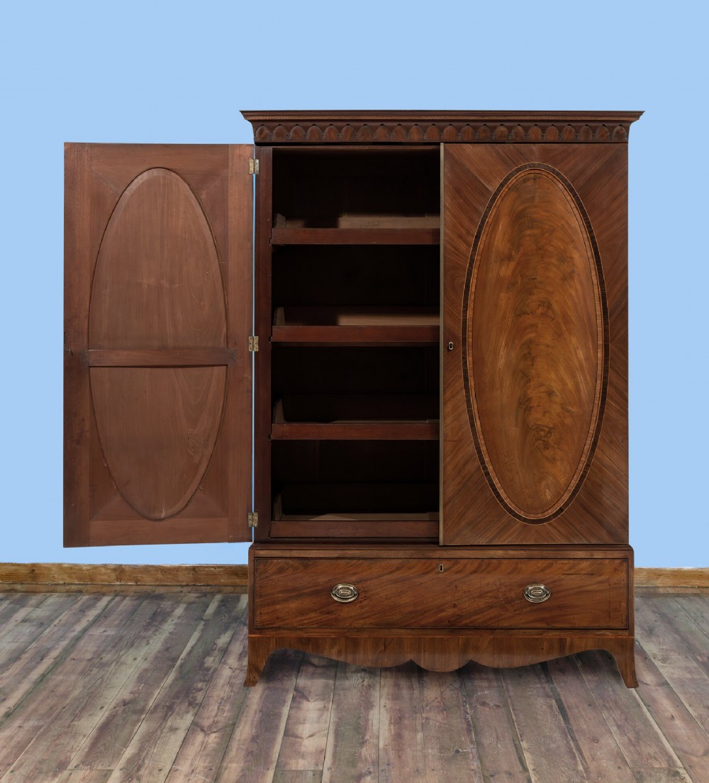 An 18th-century Hepplewhite mahogany clothes press featuring double doors with flame mahogany oval panels over a single long base drawer. View II