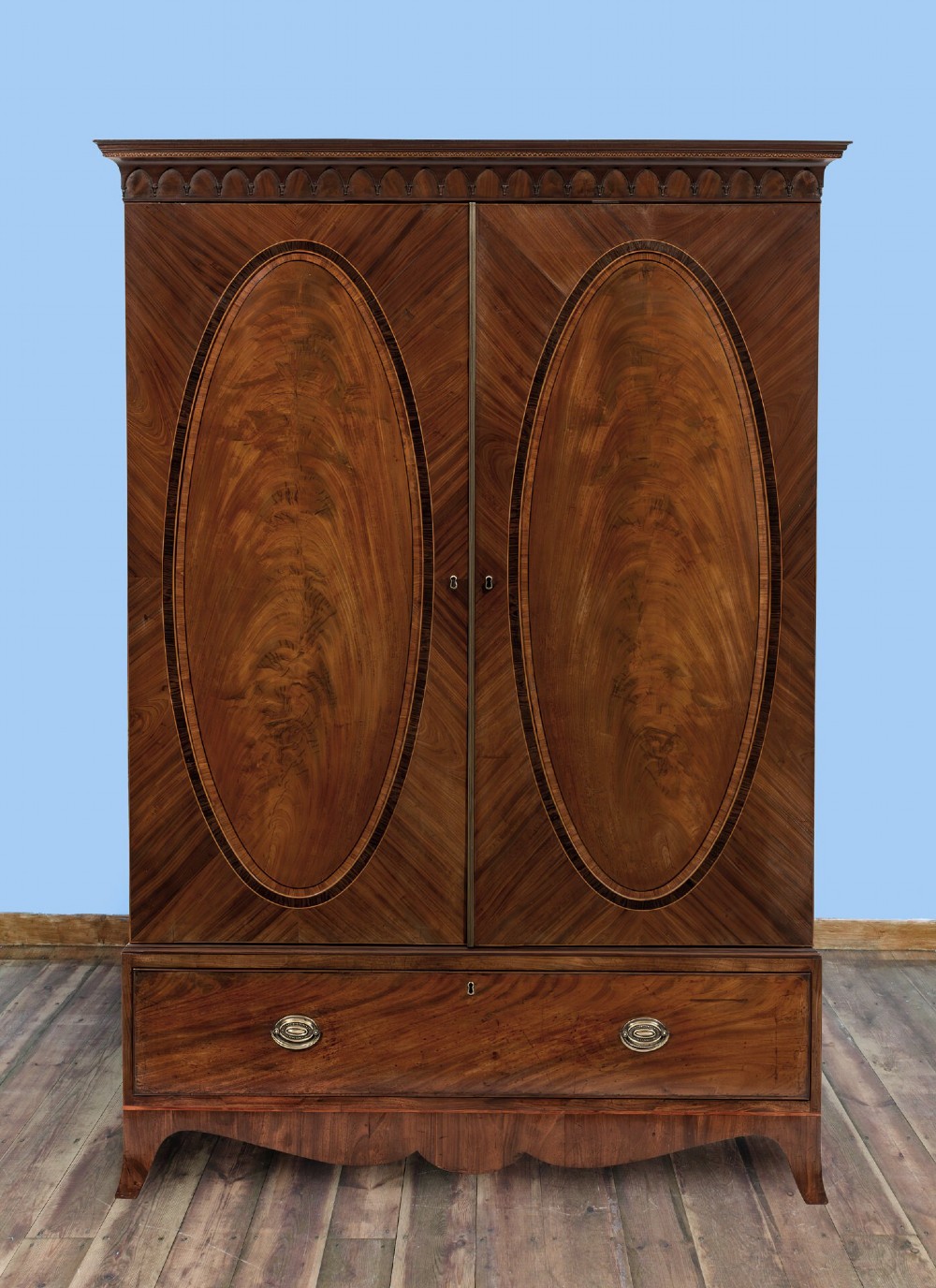 An 18th-century Hepplewhite mahogany clothes press featuring double doors with flame mahogany oval panels over a single long base drawer. View IV