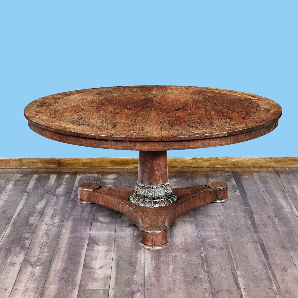 A circular George IV mahogany dining table featuring a sunburst veneer top and a central pedestal on a carved triform base.