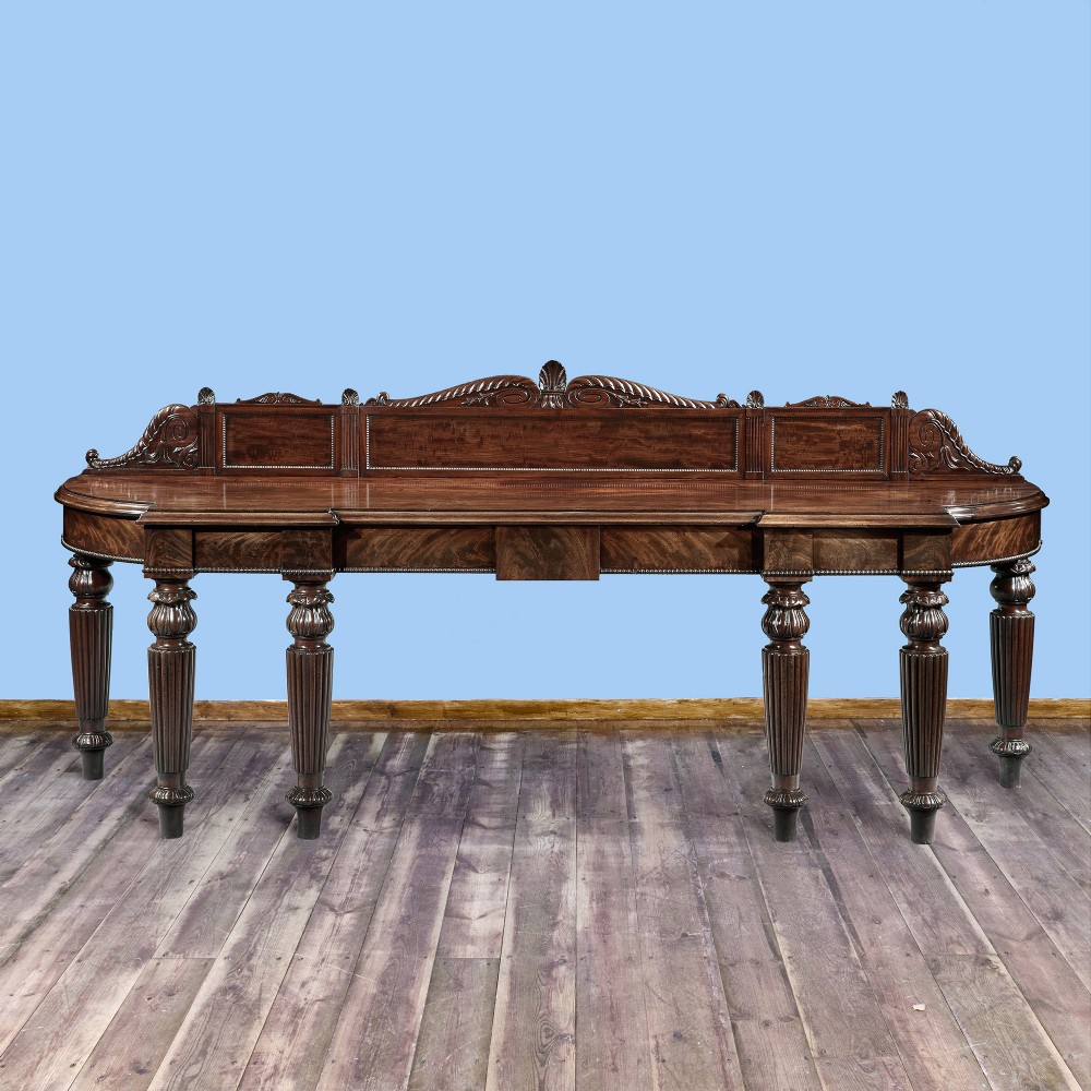 A grand George IV flame mahogany serving table featuring six reeded turned legs and a carved back gallery.