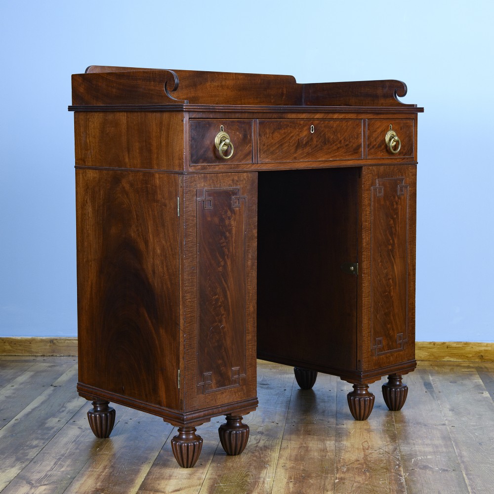 A 19th-century flame mahogany kneehole cabinet featuring brass ring handles, panelled side pedestal doors, and turned reeded feet. View IV