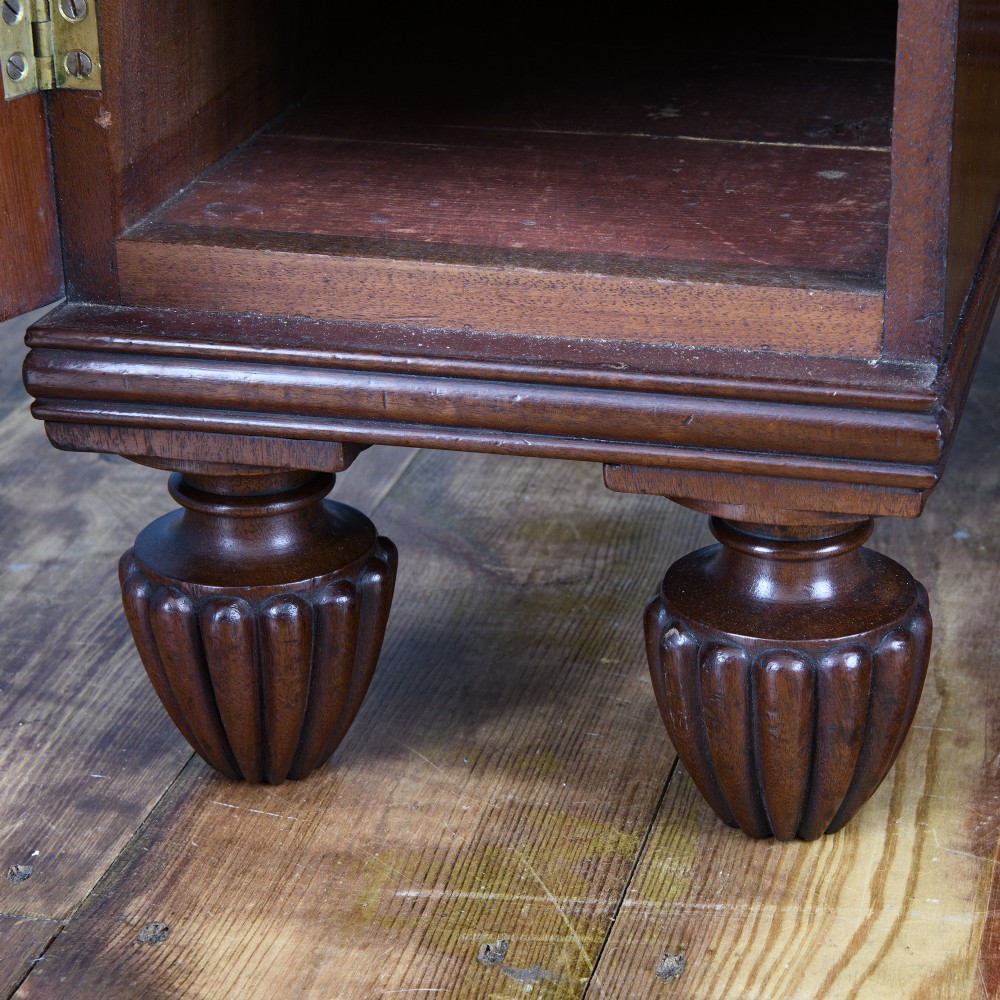 A 19th-century flame mahogany kneehole cabinet featuring brass ring handles, panelled side pedestal doors, and turned reeded feet. View VI