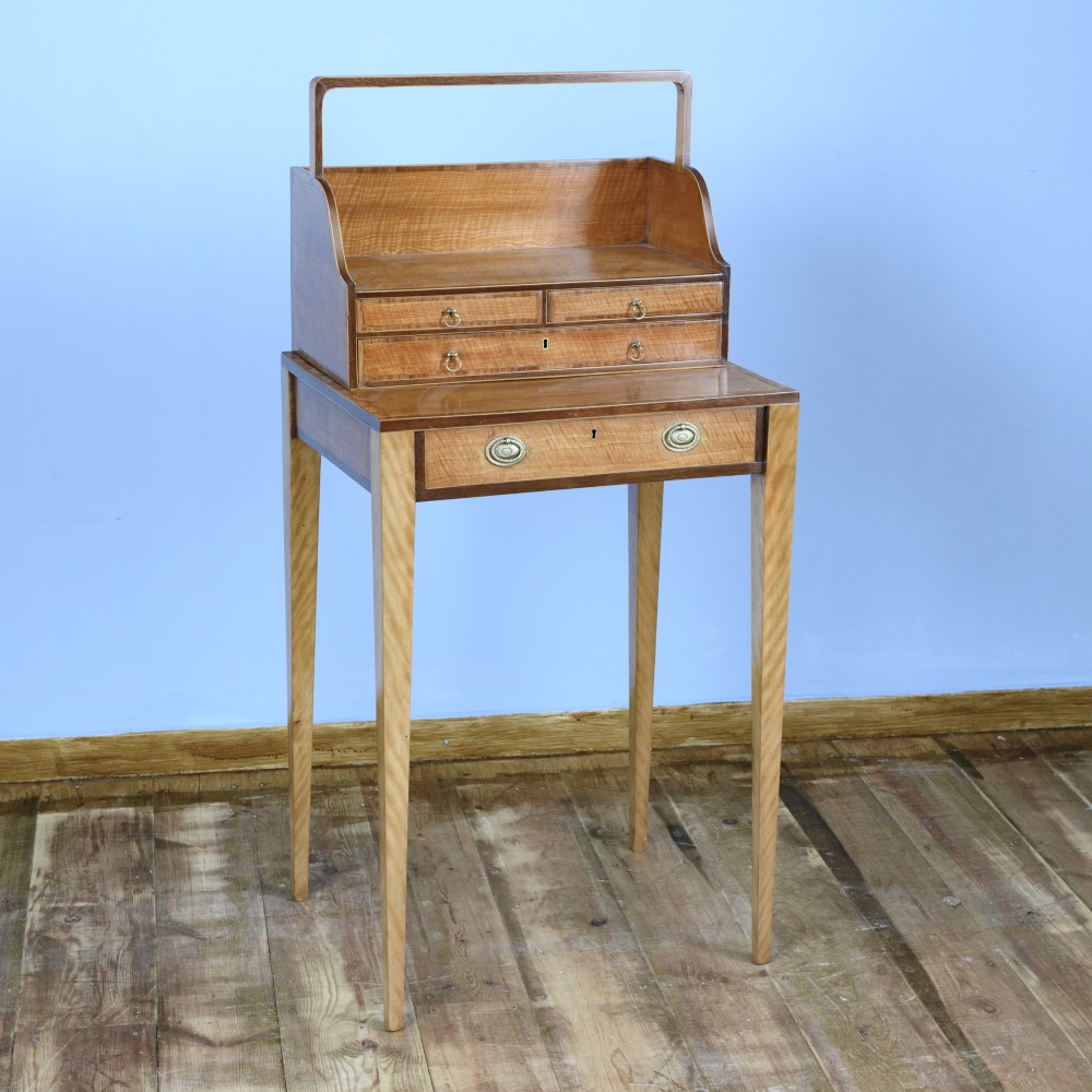 An 18th-century Georgian satinwood cheveret writing table featuring slender square tapered legs, brass ring pulls, and a upper cabinet with an integrated handle. View III