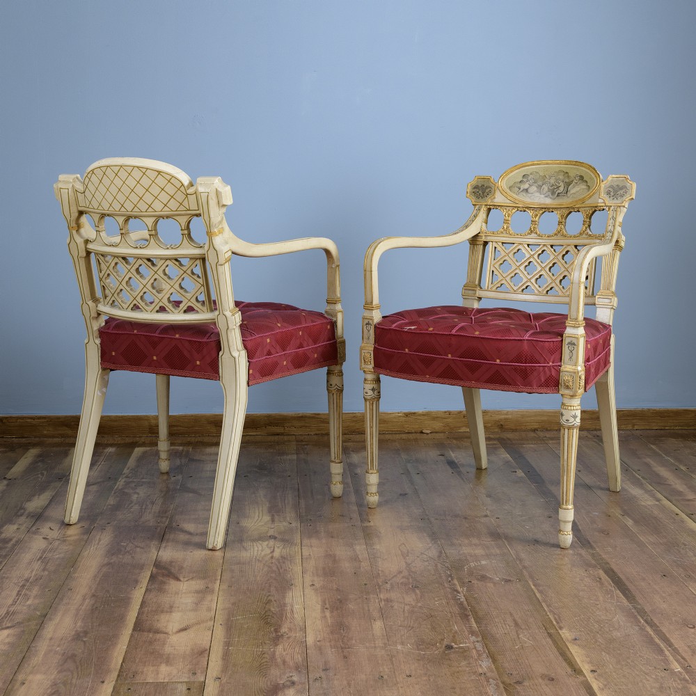 A pair of cream-painted and parcel-gilt Neoclassical armchairs featuring pierced lattice backs, painted oval medallions, and crimson fabric seats. View II