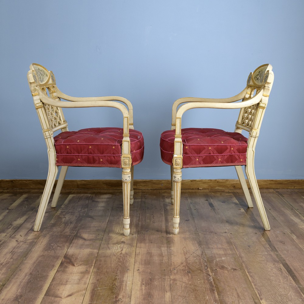 A pair of cream-painted and parcel-gilt Neoclassical armchairs featuring pierced lattice backs, painted oval medallions, and crimson fabric seats. View III