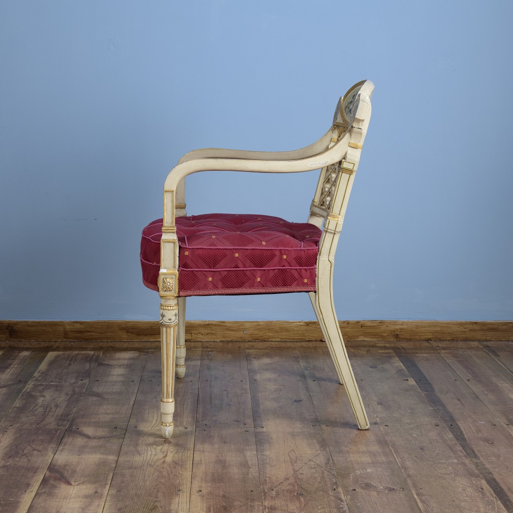 A pair of cream-painted and parcel-gilt Neoclassical armchairs featuring pierced lattice backs, painted oval medallions, and crimson fabric seats. View IV