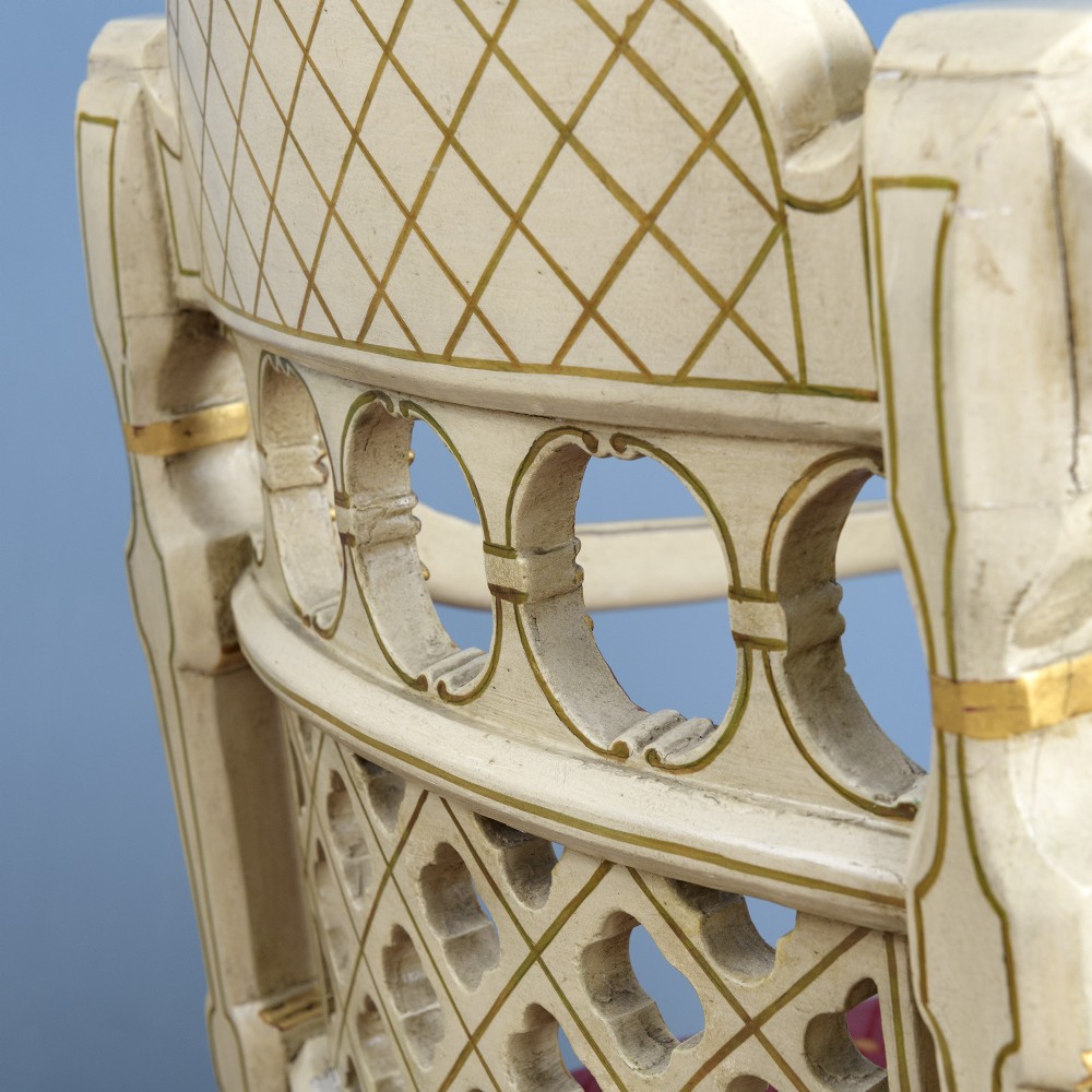 A pair of cream-painted and parcel-gilt Neoclassical armchairs featuring pierced lattice backs, painted oval medallions, and crimson fabric seats. View V