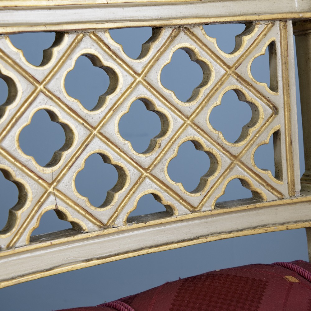 A pair of cream-painted and parcel-gilt Neoclassical armchairs featuring pierced lattice backs, painted oval medallions, and crimson fabric seats. View VII