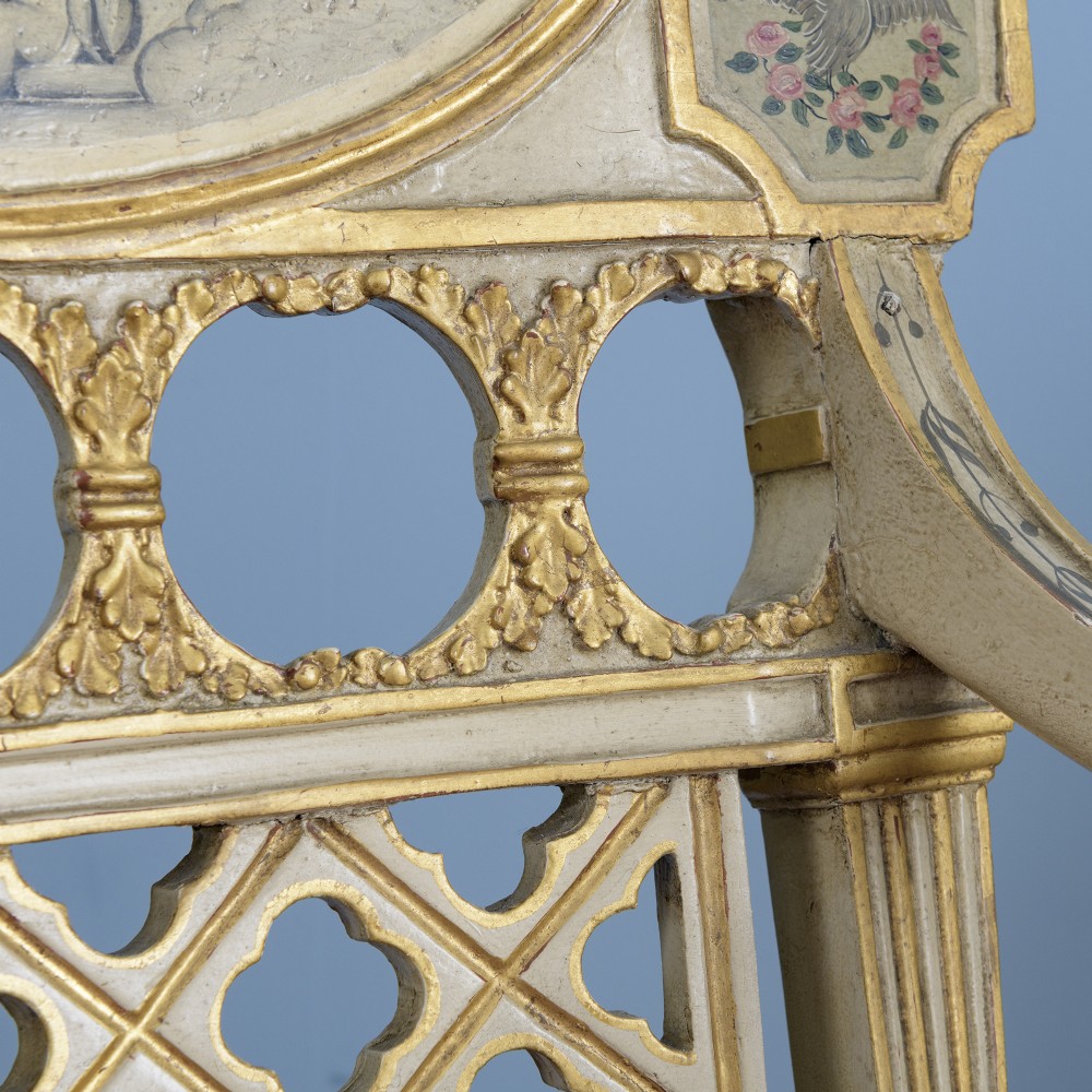 A pair of cream-painted and parcel-gilt Neoclassical armchairs featuring pierced lattice backs, painted oval medallions, and crimson fabric seats. View VIII