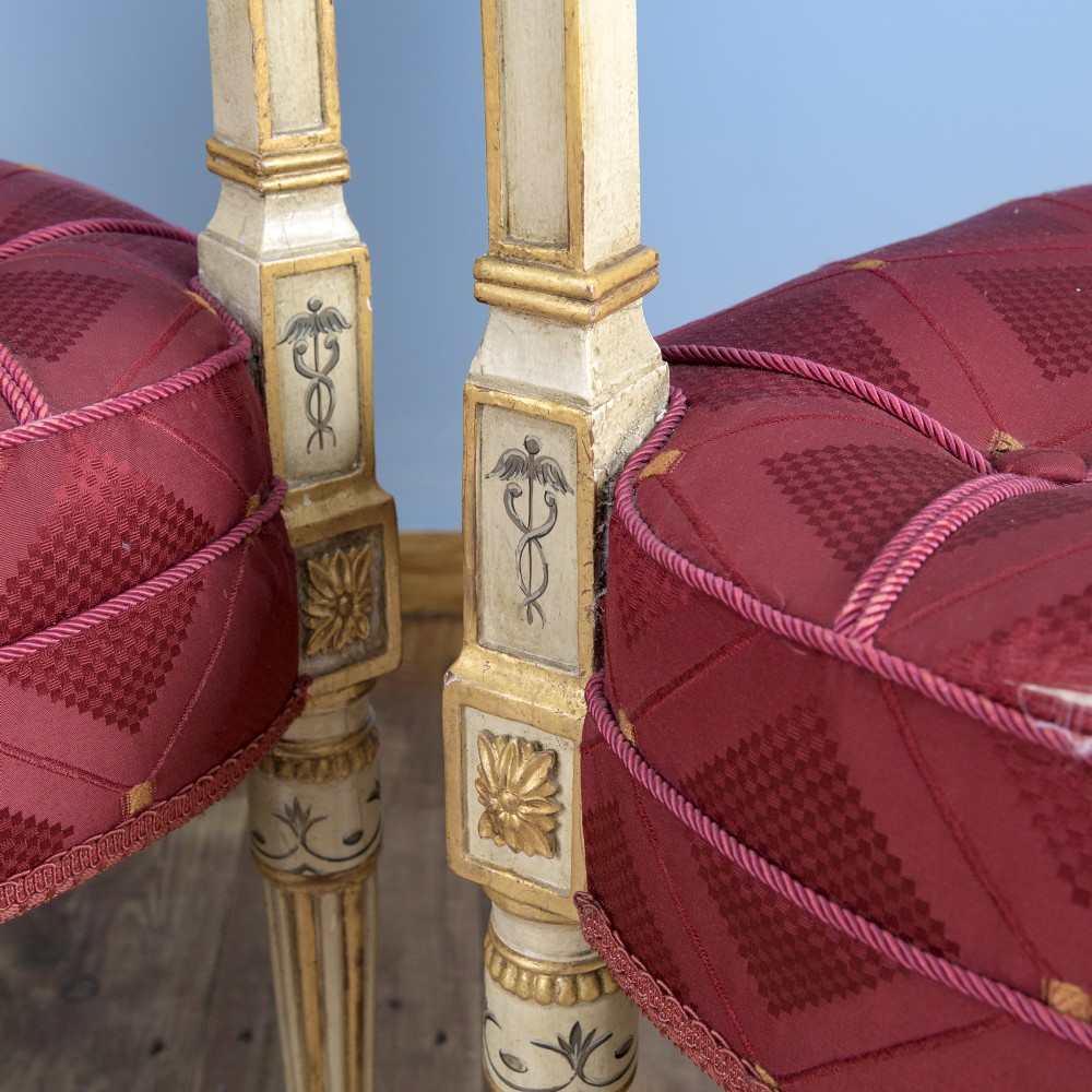 A pair of cream-painted and parcel-gilt Neoclassical armchairs featuring pierced lattice backs, painted oval medallions, and crimson fabric seats. View IX