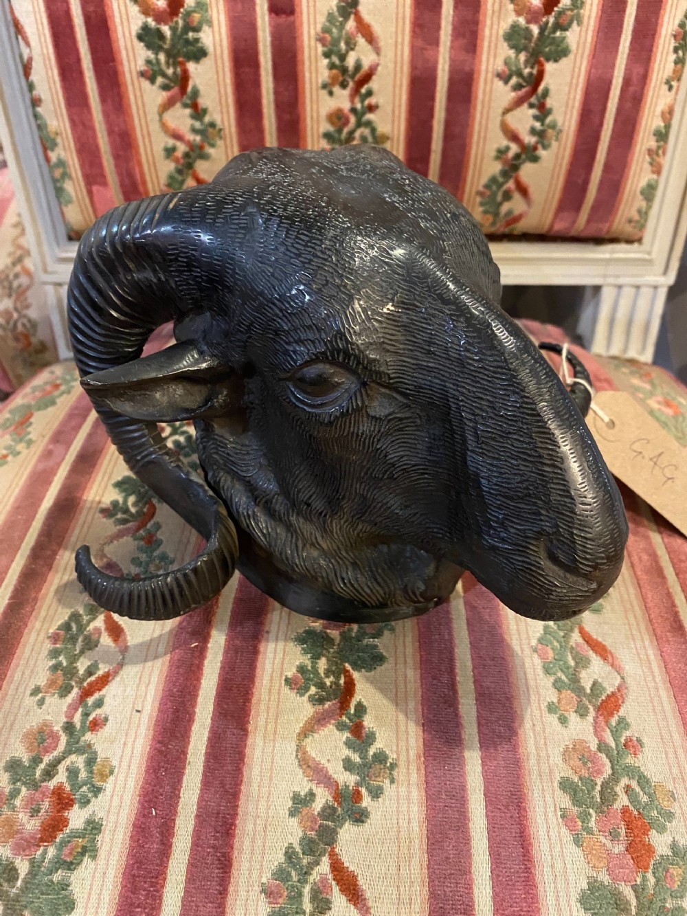 A dark patinated bronze sculpture depicting a rams head with curled ribbed horns and textured fleece.