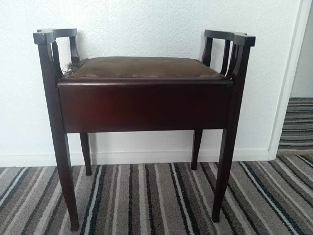 An Edwardian dark mahogany piano stool featuring raised side handles, square tapered legs, and a padded fabric lift-up seat.