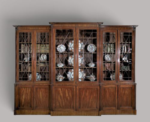 fig 1. A large George III mahogany breakfront bookcase with a central pediment, glazed upper doors with geometric glazing bars, and flame mahogany cupboard doors below.
