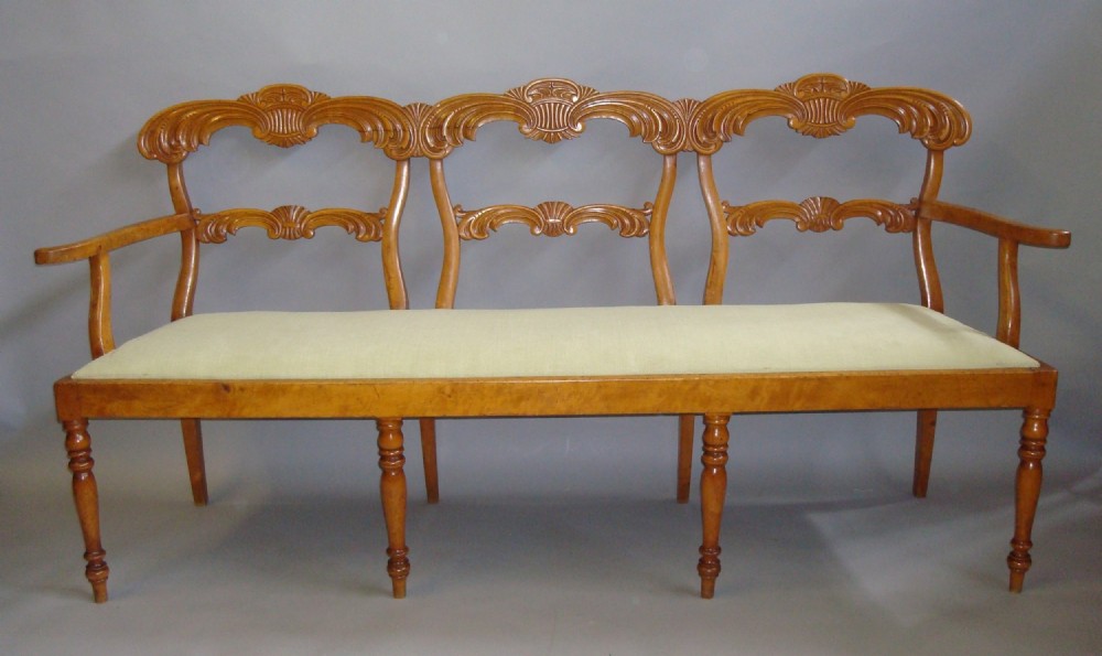 A nineteenth-century maple chair-back settee with three carved shell-motif backrests, curved armrests, turned front legs, and a light-coloured upholstered seat.