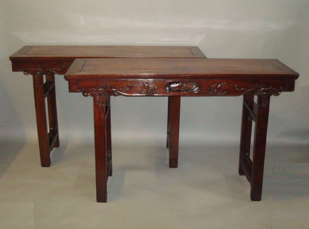 A pair of 19th-century Chinese dark hongmu wood altar tables with carved aprons and straight square legs joined by double stretchers.