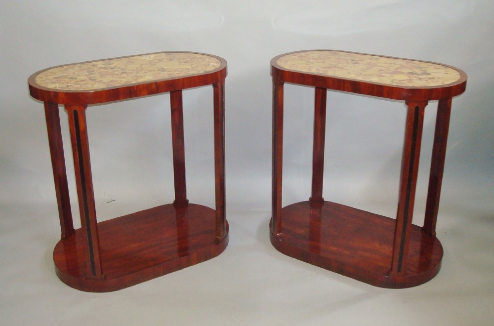 A pair of 19th-century oval mahogany side tables featuring inset variegated cream marble tops and solid lower plinth bases.