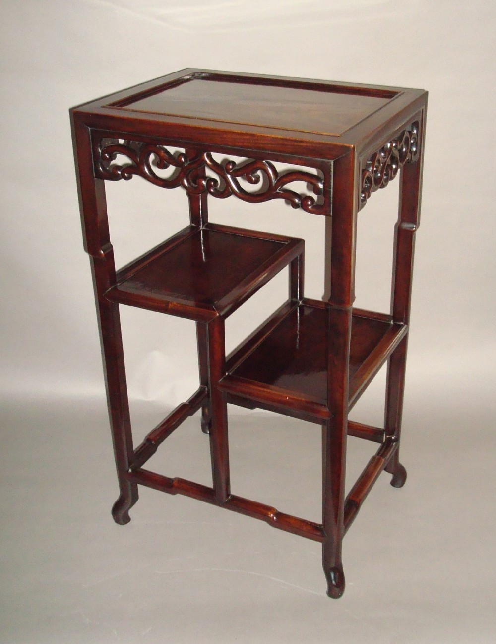 A 19th-century Chinese dark Hongmu hardwood stand table featuring carved openwork aprons, tiered shelves, and bamboo-style legs.