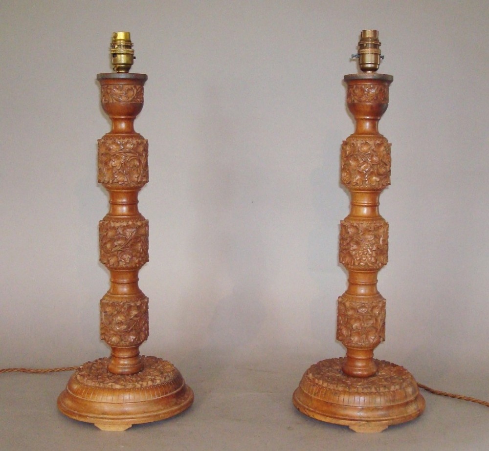A pair of turned and hand-carved walnut table lamp bases featuring cylindrical carved sections with floral patterns and circular bases.