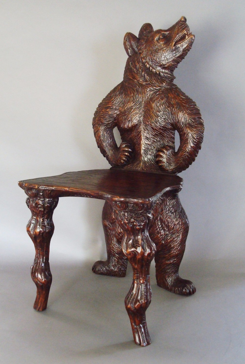 A nineteenth-century carved dark timber hall chair featuring a standing bear as the backrest and branch-form front legs.
