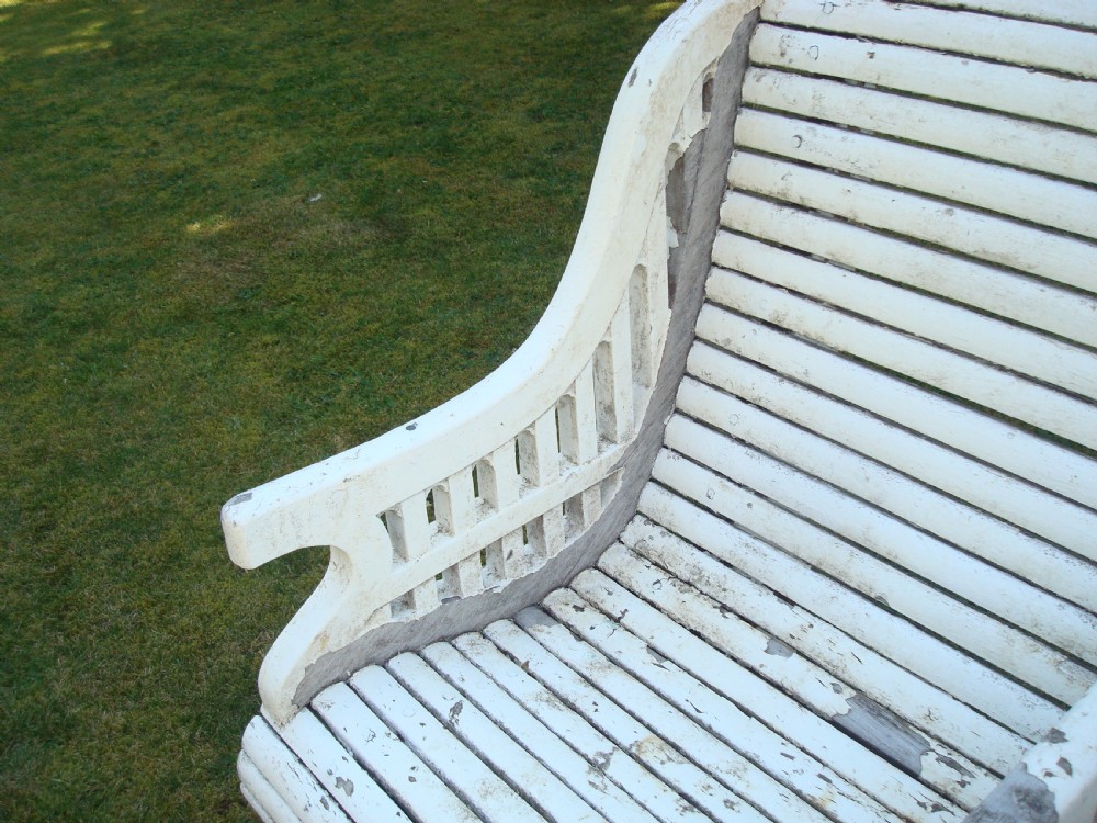 A distressed white painted slatted teak garden seat featuring a curved backrest, central divider armrest, and lattice detailed sides. View IX