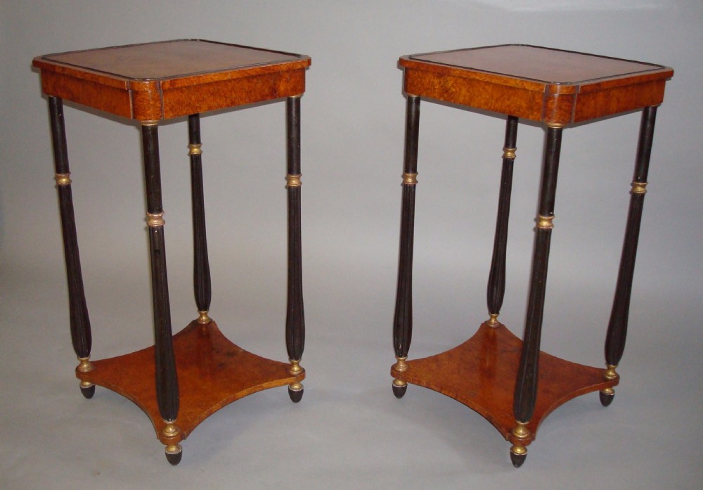A pair of tall Regency occasional tables featuring square amboyna tops, ebonised turned legs with gilt accents, and concave undertiers.