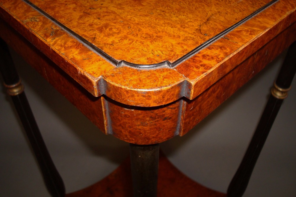 A pair of tall Regency occasional tables featuring square amboyna tops, ebonised turned legs with gilt accents, and concave undertiers. View X