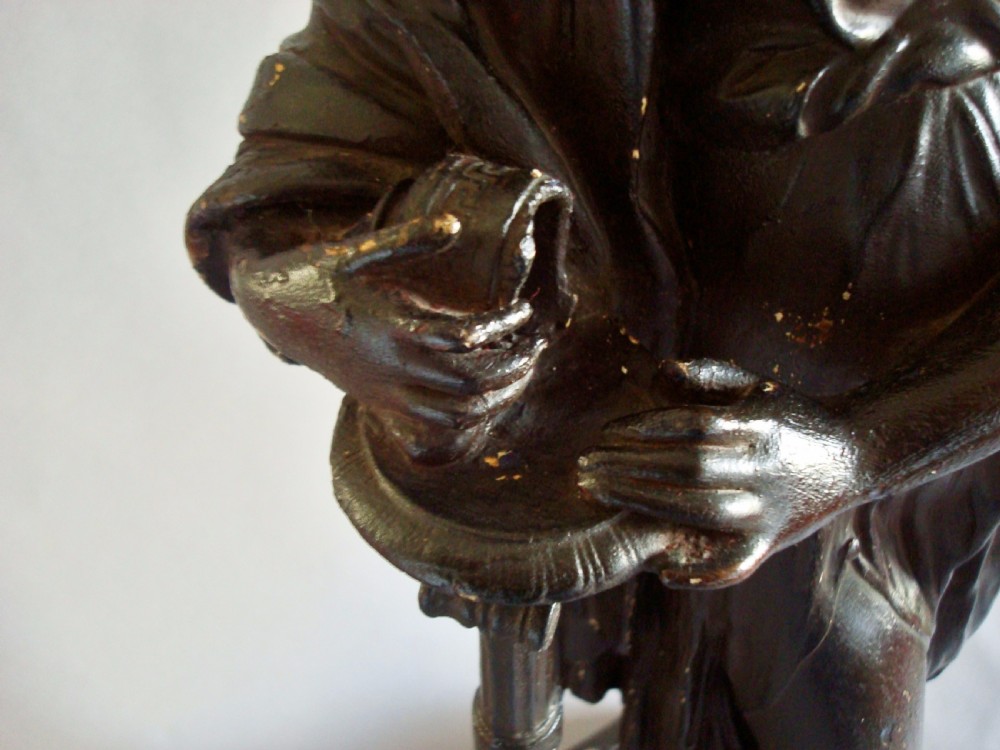 A dark bronzed plaster sculpture depicting a draped classical female figure standing beside a decorative column on a rectangular pedestal. View VIII