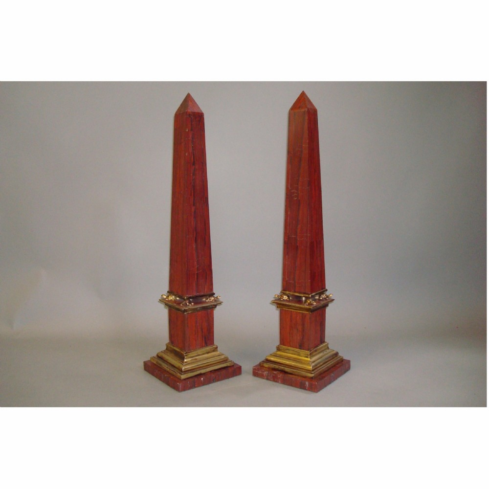 A pair of red marble obelisks featuring gilt metal collars and stepped bases.