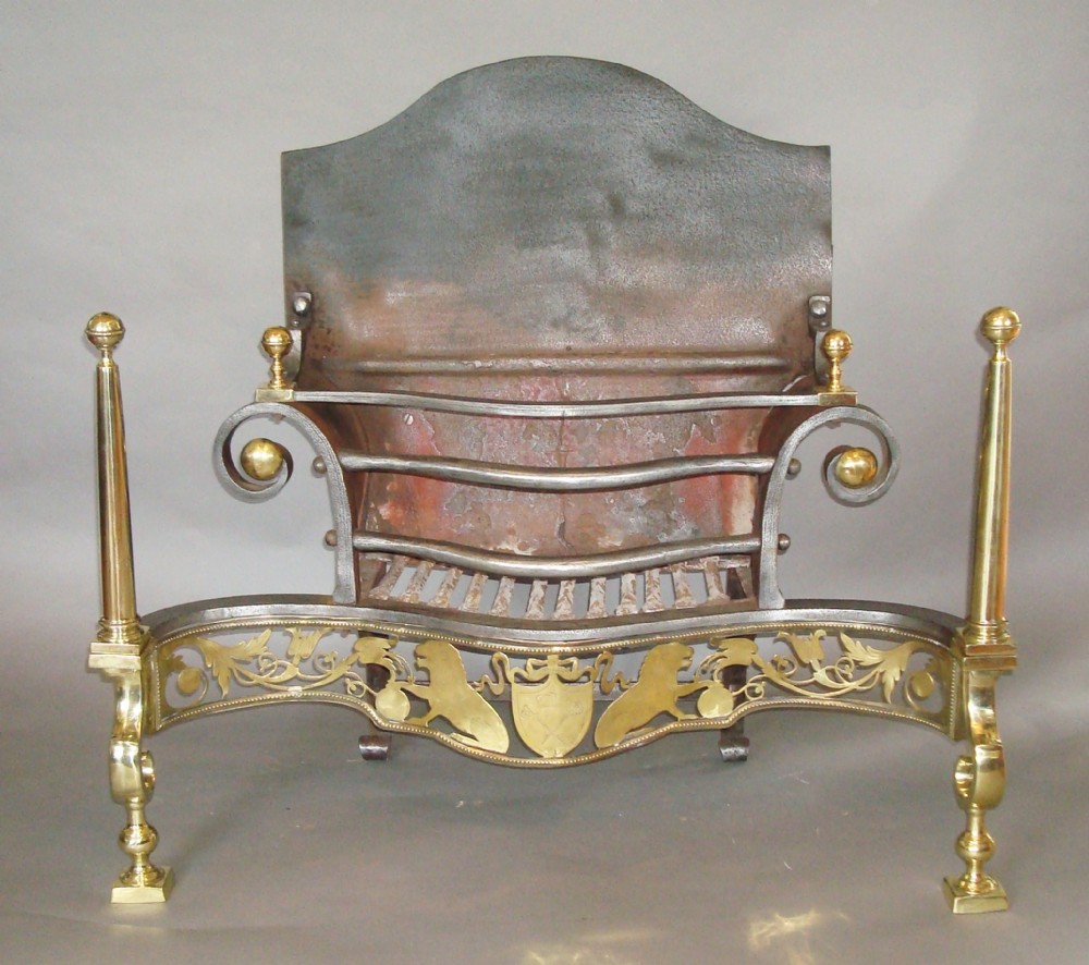 A 19th-century Neoclassical style fire grate constructed from black iron with a scroll-ended basket, flanked by polished brass columns and an ornate pierced brass apron featuring lion motifs.