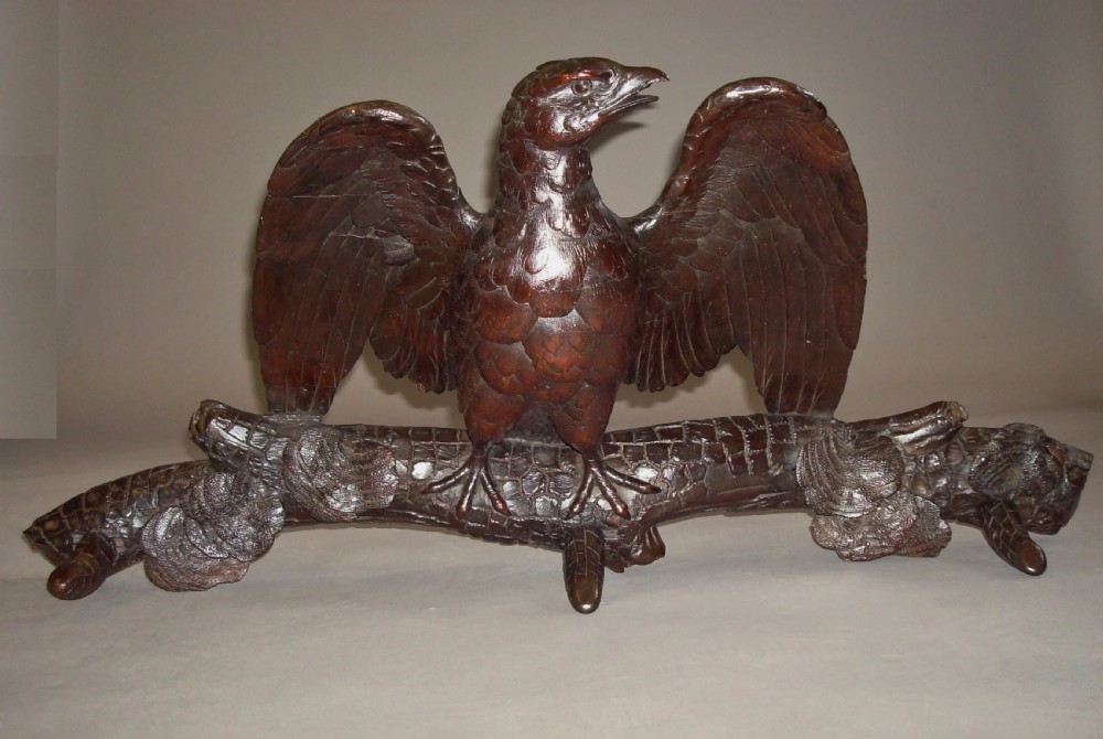 A 19th-century dark carved wood coat rack featuring an eagle with outstretched wings perched on a rustic branch with integral hanging pegs.