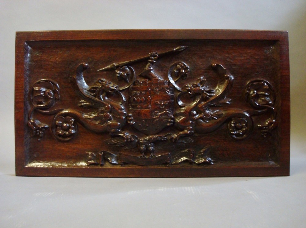 A rectangular carved dark walnut panel featuring a central coat of arms flanked by mythical beasts and foliate scrollwork.