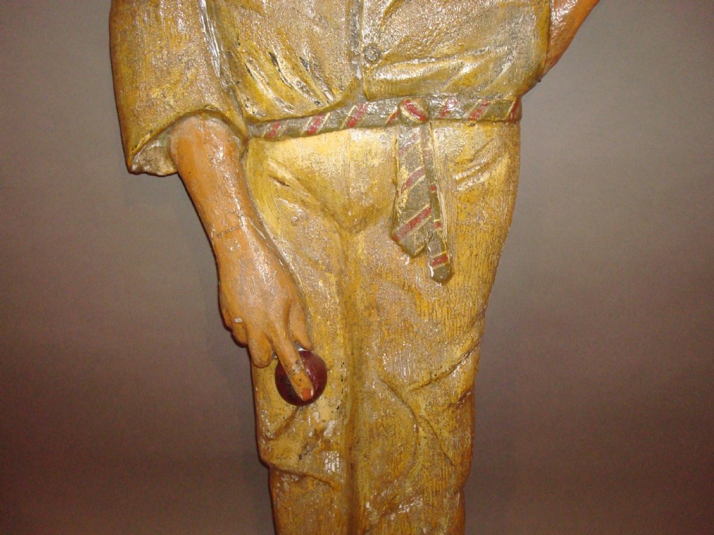 A life-size early 20th-century carved wood figure of a cricketer wearing a hat, shirt, trousers, and holding a ball. View VI