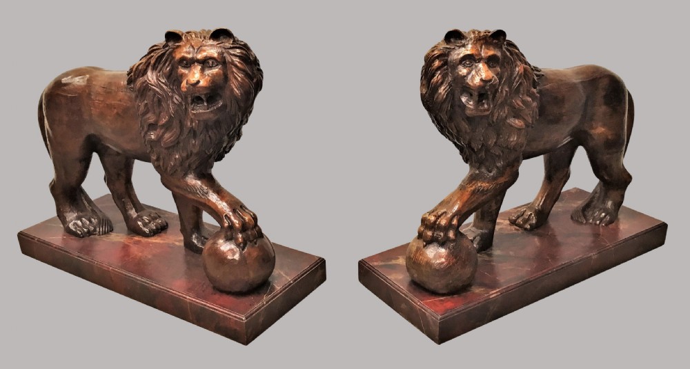 A pair of nineteenth-century carved wooden Medici lions depicted standing with one paw resting on a sphere, mounted on reddish marbled rectangular bases.
