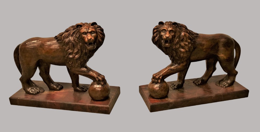 A pair of nineteenth-century carved wooden Medici lions depicted standing with one paw resting on a sphere, mounted on reddish marbled rectangular bases. View II
