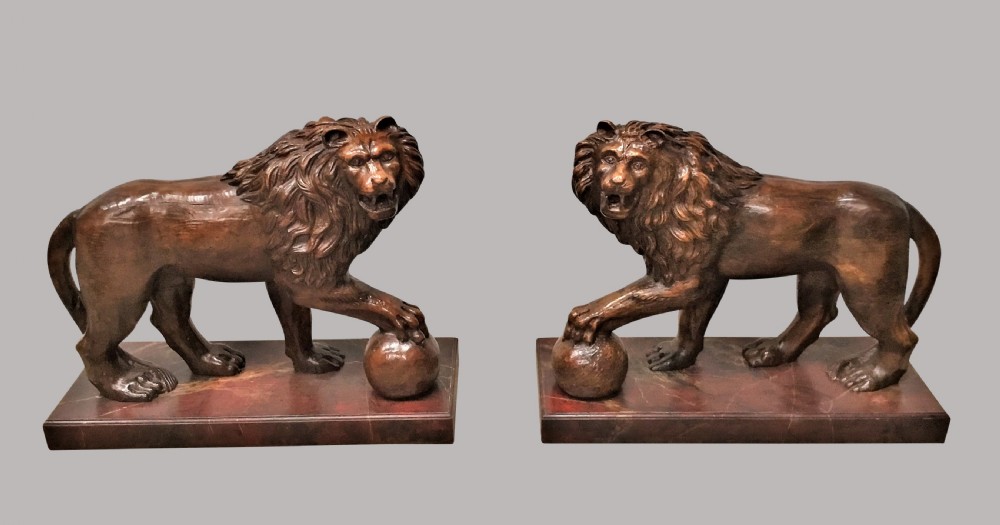 A pair of nineteenth-century carved wooden Medici lions depicted standing with one paw resting on a sphere, mounted on reddish marbled rectangular bases. View III