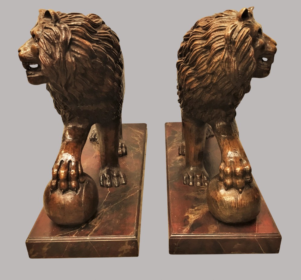 A pair of nineteenth-century carved wooden Medici lions depicted standing with one paw resting on a sphere, mounted on reddish marbled rectangular bases. View IV