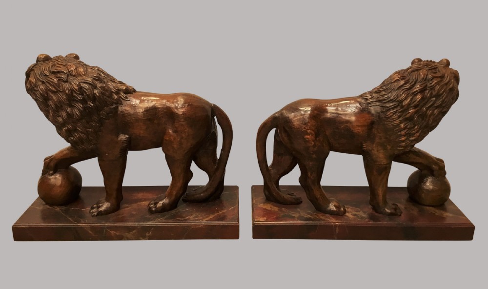 A pair of nineteenth-century carved wooden Medici lions depicted standing with one paw resting on a sphere, mounted on reddish marbled rectangular bases. View X