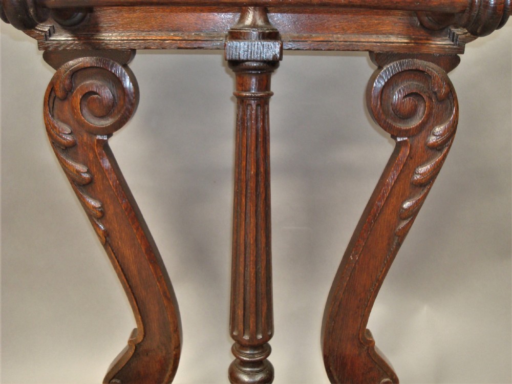An antique dark oak stick stand featuring scroll support arms, a carved top cresting, a central column, and a removable metal drip tray at the base. View XI