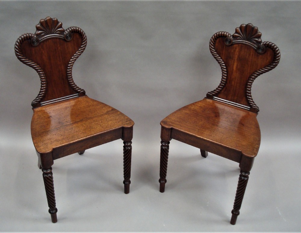 A pair of Regency mahogany hall chairs featuring carved shell cresting, rope-twist backrest borders, solid seats, and spiral-turned front legs. View IV
