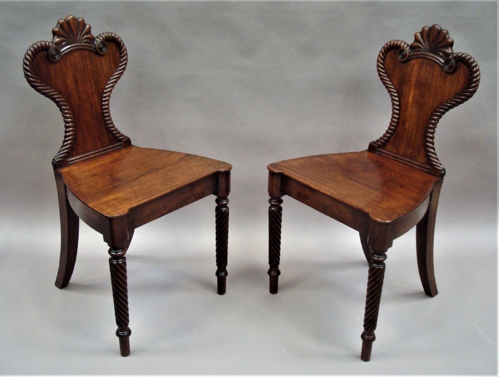A pair of Regency mahogany hall chairs featuring carved shell cresting, rope-twist backrest borders, solid seats, and spiral-turned front legs. View V