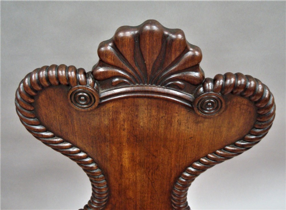 A pair of Regency mahogany hall chairs featuring carved shell cresting, rope-twist backrest borders, solid seats, and spiral-turned front legs. View IX