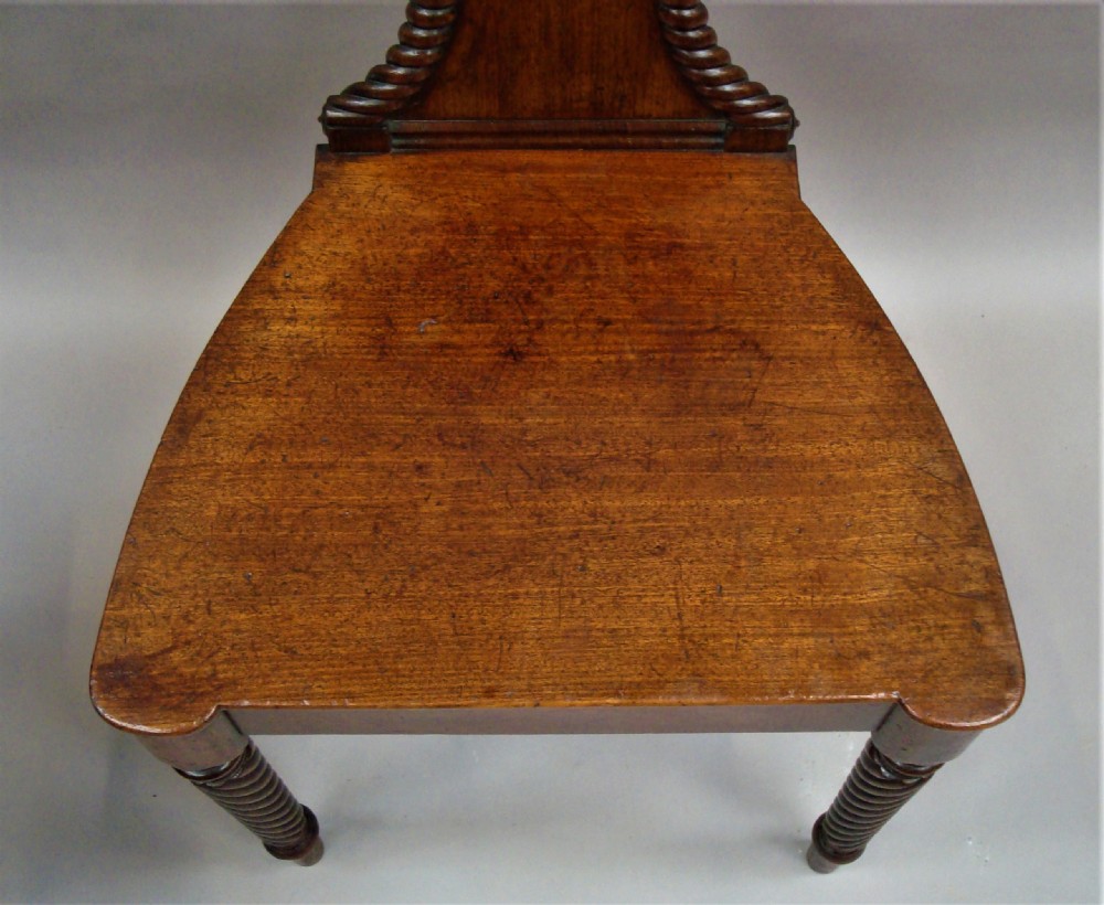 A pair of Regency mahogany hall chairs featuring carved shell cresting, rope-twist backrest borders, solid seats, and spiral-turned front legs. View XVII