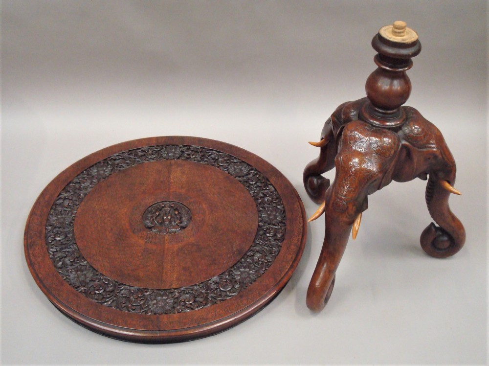 A 19th-century carved teak round table supported by a tripod base shaped like three elephant heads with curving trunks. View XIV