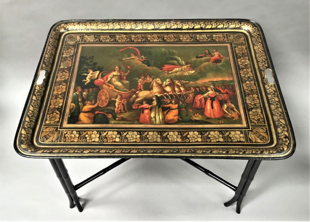 A large Regency painted toleware tray featuring a classical mythological scene and gilded borders, mounted on a black faux bamboo cross-leg stand. View IV