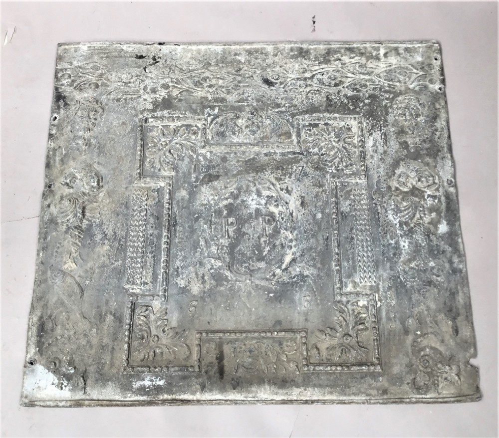 A square cast lead panel dated 1765 featuring a central wreath with monogram PP, acanthus scroll borders, cherub detail, and side relief motifs of dolphins. View IX