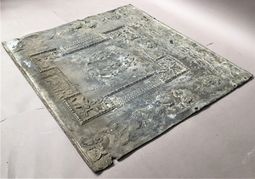 A square cast lead panel dated 1765 featuring a central wreath with monogram PP, acanthus scroll borders, cherub detail, and side relief motifs of dolphins. View XVII