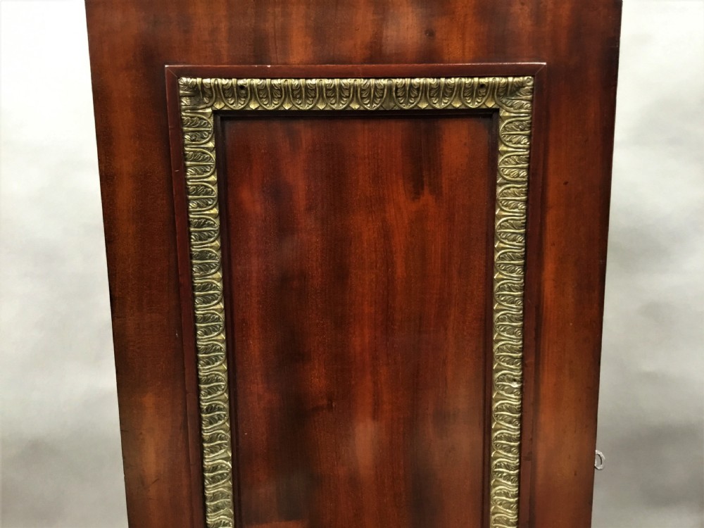A tall mahogany Regency pedestal cabinet featuring cast brass leaf borders and a single panelled door on a plinth base. View XII