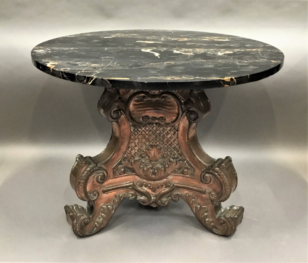 A round black marble low centre table featuring light veining, supported by an ornate copper pedestal base with scrolled feet and carved motifs.